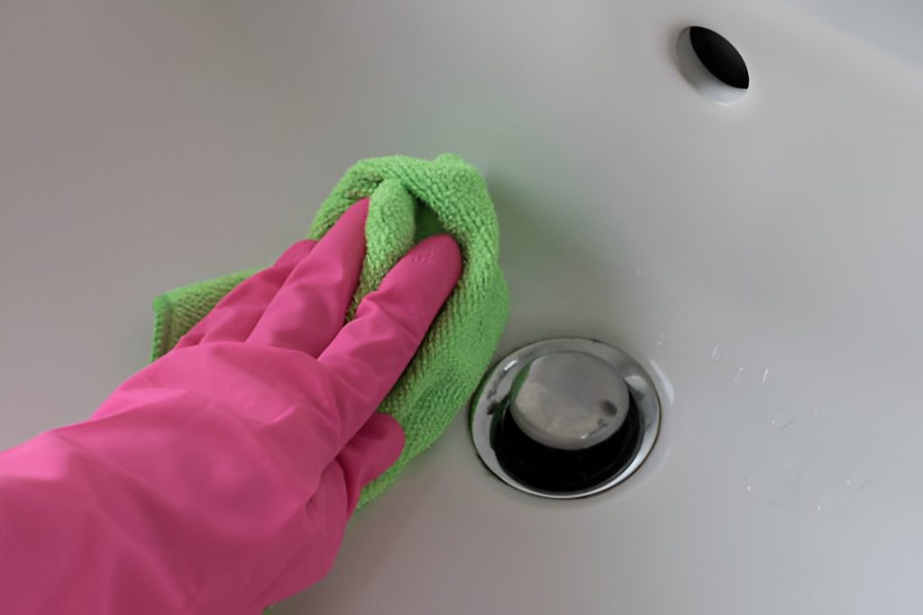 close-up of a hand in a pink glove wiping a bathroom sink